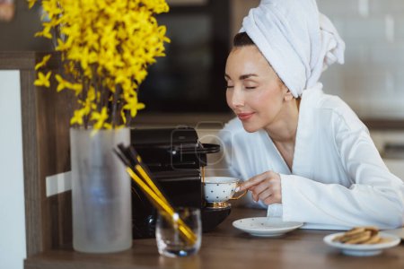 Téléchargez les photos : Jeune femme en peignoir faire une tasse de café et profiter de l'odeur de café savoureux sur la cuisine à la maison. - en image libre de droit