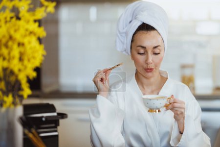 Foto de Una joven atractiva disfrutando de un café de la mañana y galletas en su cocina en casa. - Imagen libre de derechos
