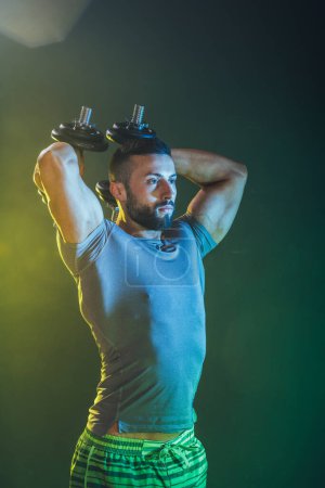 Photo for Shot of a muscular bodybuilder doing hard training with dumbbells. He is pumping up his triceps muscle with heavy weight. - Royalty Free Image