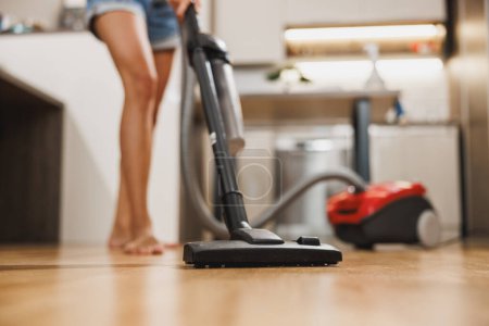 Tournage d'une femme qui nettoie une maison. Elle nettoie efficacement un plancher de bois dur avec un aspirateur puissant.