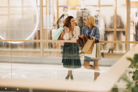 Téléchargez les photos : Tourné de deux jolies femmes souriantes qui prennent un peu de temps pour profiter d'une virée shopping dans le centre commercial de la ville. - en image libre de droit