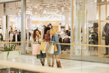 Foto de Fotografía de tres atractivas mujeres divirtiéndose juntas en un centro comercial mientras salen de compras durante las ventas de Black Friday o Cyber Monday. - Imagen libre de derechos