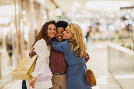 Téléchargez les photos : Plan recadré de trois copines souriantes se serrent dans leurs bras tout en prenant un peu de temps pour profiter d'une virée shopping dans le centre commercial de la ville. - en image libre de droit