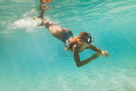 Photo for A beautiful young woman is having fun at summer vacation exploring seafloor during scuba diving in sea. - Royalty Free Image