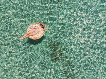 Téléchargez les photos : Vue aérienne d'une belle femme qui nage sur le grand beignet gonflable dans la mer turquoise transparente. Vue du dessus du drone. - en image libre de droit