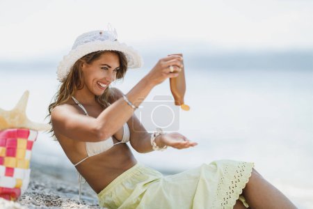 Photo for An attractive young woman is using sun protection cream and enjoying time on the beach. - Royalty Free Image
