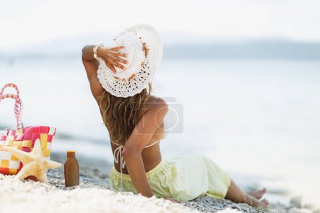 Téléchargez les photos : Vue arrière sur une jolie femme en bikini, avec chapeau d'été, est assis et profiter à la plage le jour d'été. - en image libre de droit