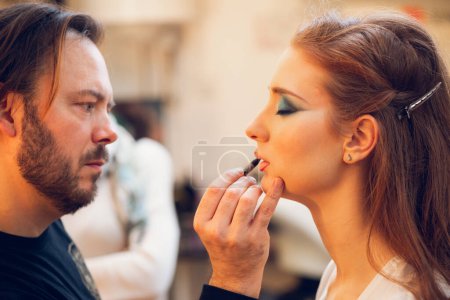 Téléchargez les photos : Maquilleur masculin prêt à appliquer le maquillage sur les lèvres d'un mannequin. - en image libre de droit