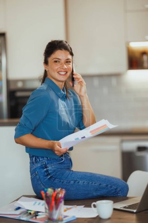Téléchargez les photos : Femme d'affaires parlant sur un smartphone tout en travaillant à partir de son bureau à domicile. - en image libre de droit