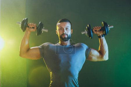 Photo for Shot of a muscular bodybuilder doing hard training with dumbbell. He is pumping up his shoulders muscle with heavy weight. - Royalty Free Image