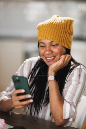 Téléchargez les photos : Femme d'affaires africaine utilisant un téléphone portable tout en prenant une pause pendant le travail à la maison. - en image libre de droit