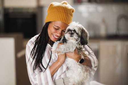 Foto de Mujer africana divirtiéndose con su mascota Shih Tzu perro en casa. - Imagen libre de derechos