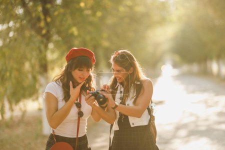 Foto de Dos hermosas mujeres jóvenes felices están caminando por la avenida soleada y mirando las fotos en la cámara. - Imagen libre de derechos