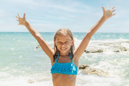 Téléchargez les photos : Petite fille mignonne s'amuser et profiter de la plage à bras ouverts et regarder la caméra. - en image libre de droit