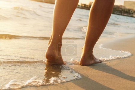 Téléchargez les photos : Gros plan d'une femme aux jambes méconnaissables marchant sur la plage de sable. Vue arrière. - en image libre de droit