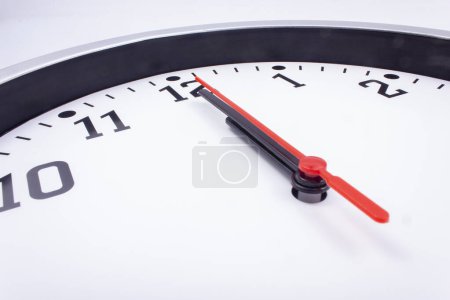 Foto de Medianoche. Reloj de oficina blanco y negro con un puntero rojo - doce en punto. - Imagen libre de derechos