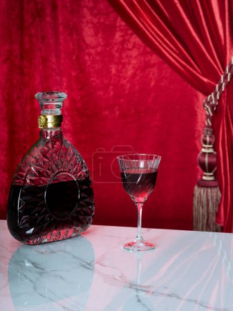 Téléchargez les photos : Vue rapprochée de la bouteille de luxe et du verre sur table en marbre avec dossier rouge - en image libre de droit