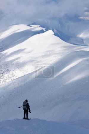 Téléchargez les photos : Homme avec sac à dos en randonnée hivernale dans les montagnes enneigées - en image libre de droit