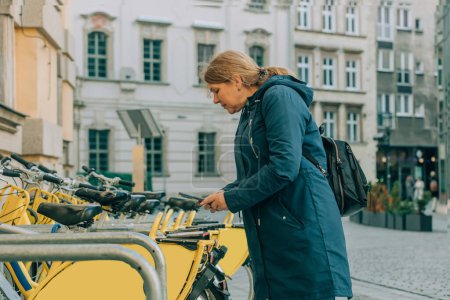 Foto de Mujer mayor tratar de alquilar una bicicleta mediante el uso de aplicación en el teléfono móvil, Wroclaw, Polonia - Imagen libre de derechos
