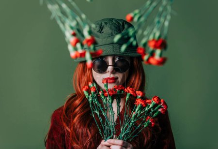 Foto de Stylish redhead woman in hat and burgundy color suit with carnations on green background - Imagen libre de derechos