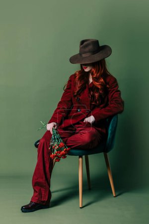 Téléchargez les photos : Stylish redhead woman in hat and burgundy color suit on green background - en image libre de droit