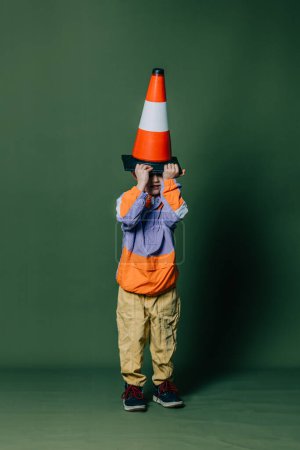 Foto de Stylish little boy with traffic cone on green background - Imagen libre de derechos