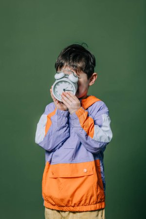 Téléchargez les photos : Stylish little boy with alarm clock on green background - en image libre de droit