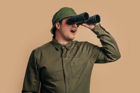 Photo for Stylish guy in boonie hat with binoculars on brown background - Royalty Free Image