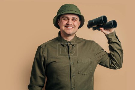 Photo pour Stylish guy in boonie hat with binoculars on brown background - image libre de droit