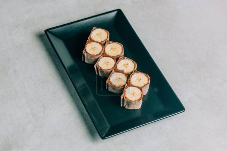 Photo for Sweet sushi rolls with banana and chocolate on black plate - Royalty Free Image