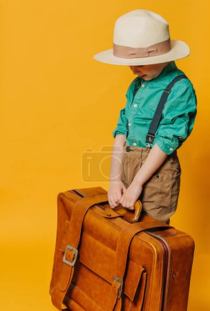 Téléchargez les photos : Petit garçon en chapeau, bretelles et chemise verte avec sac sur fond jaune - en image libre de droit
