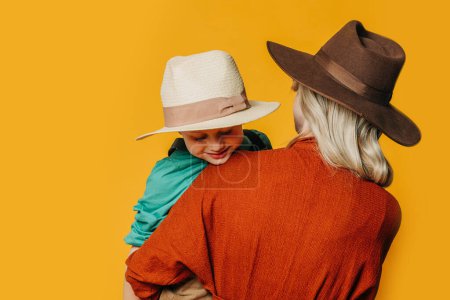 Téléchargez les photos : Vue de face arrière sur la mère et le fils élégants en vêtements vintage sur fond jaune - en image libre de droit