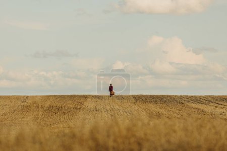 Foto de Elegante mujer con sombrero vintage abrigo rojo con maleta en el campo de trigo en el campo - Imagen libre de derechos