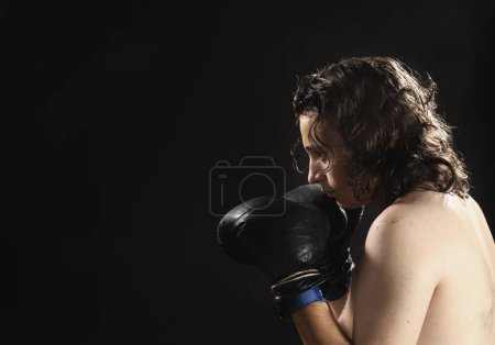 Téléchargez les photos : Un jeune homme boxe sur le noir - en image libre de droit