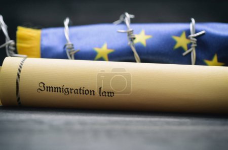 Bandera de la Unión Europea, alambre de púas y ley de inmigración sobre fondo de madera negra, concepto de migración
.
