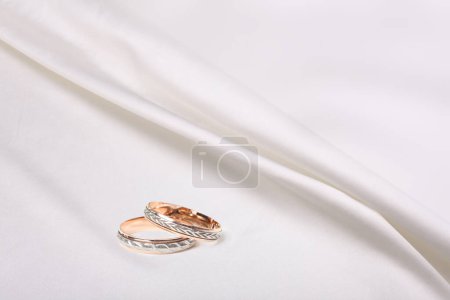 Téléchargez les photos : Anneaux de mariage sur tissu ondulé blanc beige nacre soie. Texture abstraite espace de copie horizontal arrière-plan. - en image libre de droit