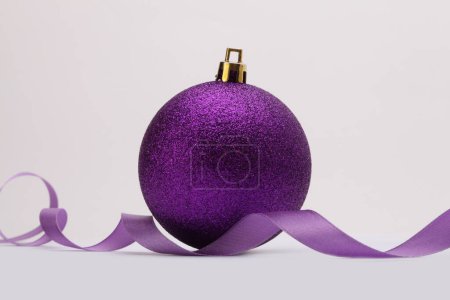 Foto de Close-up Violeta brillo textura nácar y brillo Feliz bola de Navidad, cinta sobre fondo beige. - Imagen libre de derechos