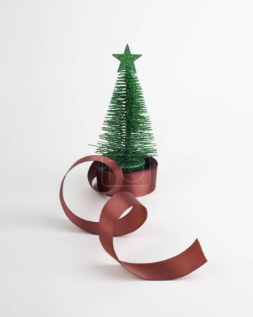 Photo for Small decorative green fir tree and brown ribbon on light  background. - Royalty Free Image