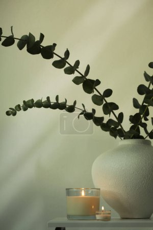 Photo for Burning candle, Leaf eucalyptus bouquet in bowl on beige interior. Selective soft focus. Minimalist still life. Light and shadow copy space background. - Royalty Free Image
