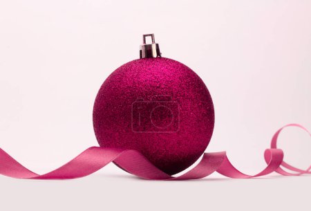 Téléchargez les photos : Gros plan magenta paillettes texture nacre et lueur Joyeux Noël boule, ruban sur fond beige. - en image libre de droit