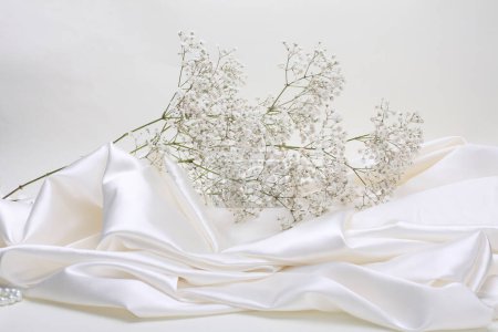 Photo for Beige pearl wave fabric silk and Gypsophila flower twig. Abstract texture horizontal copy space background. - Royalty Free Image