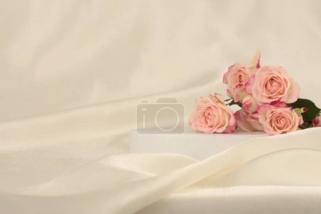 Photo for Pink rose flower bouquet on white podium and silk fabric.. Light beige background. Minimal empty display product presentation scene. - Royalty Free Image