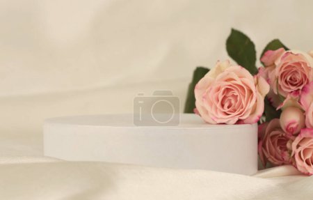Téléchargez les photos : Bouquet de fleurs de rose sur podium blanc et tissu de soie.. Fond beige clair. Scène de présentation minimale du produit d'affichage vide. - en image libre de droit