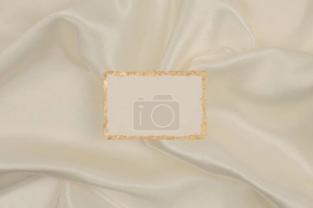Foto de Brillo dorado marco de papel de lona vacío sobre fondo de tela de seda beige. Textura abstracta del espacio de copia. - Imagen libre de derechos