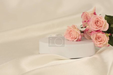 Téléchargez les photos : Bouquet de fleurs de rose sur podium blanc et tissu de soie.. Fond beige clair. Scène de présentation minimale du produit d'affichage vide. - en image libre de droit