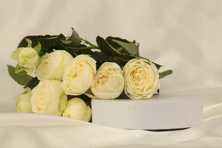 Photo for Yellow rose flower bouquet on white podium and silk fabric. Light beige background. Minimal empty display product presentation scene. - Royalty Free Image
