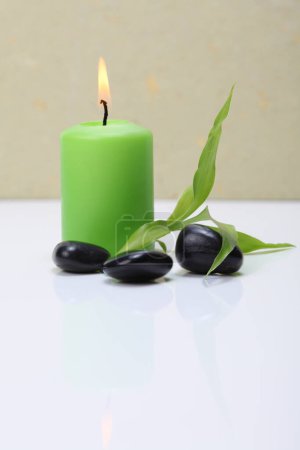 Photo for Burning green candle, black stones and bamboo leaf. - Royalty Free Image