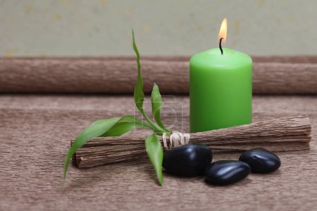 Photo for Burning green candle, black stones and bamboo leaf on brown mat  background. - Royalty Free Image