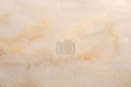 Beige, gold glitter ink watercolor smoke flow stain blot on wet paper grain texture background.