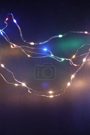 Téléchargez les photos : Doux foyer fumée flou Noël couleur guirlande lumières sur fond de mur sombre. - en image libre de droit